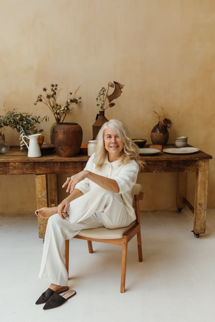 A senior woman seated in a bright room with rustic decor, exuding elegance and relaxation.